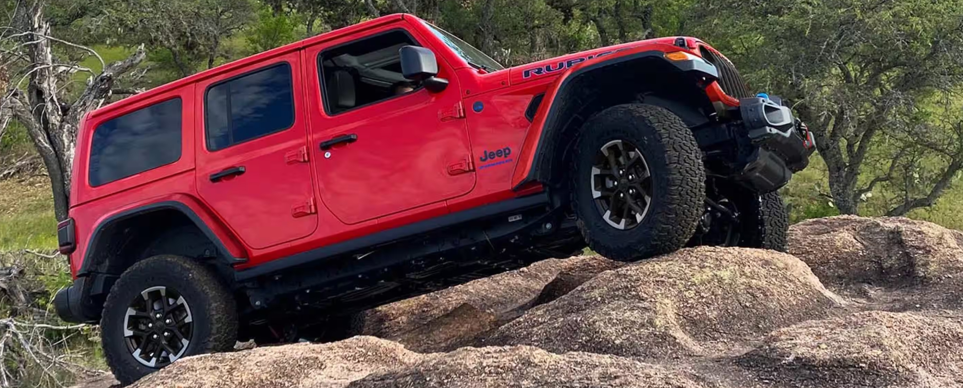 Red Jeep Wrangler driving on a rocky hill